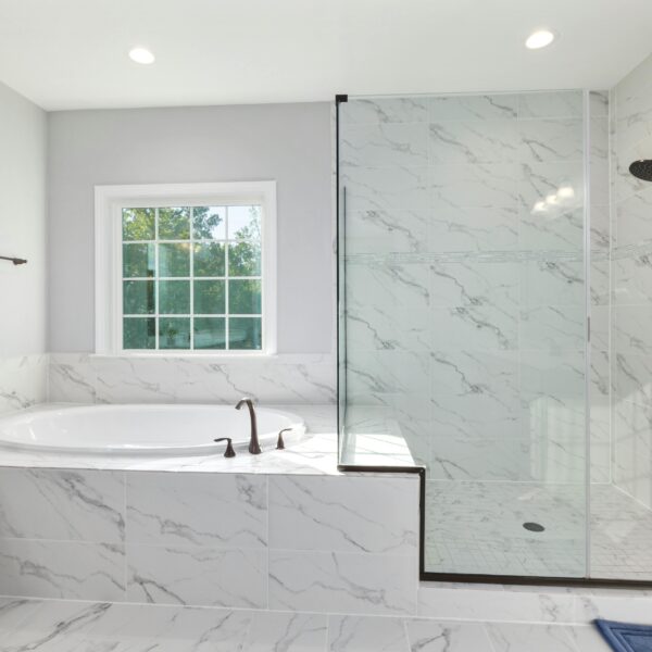 Elegant minimalist bathroom featuring a marble bathtub and glass shower with modern fixtures.
